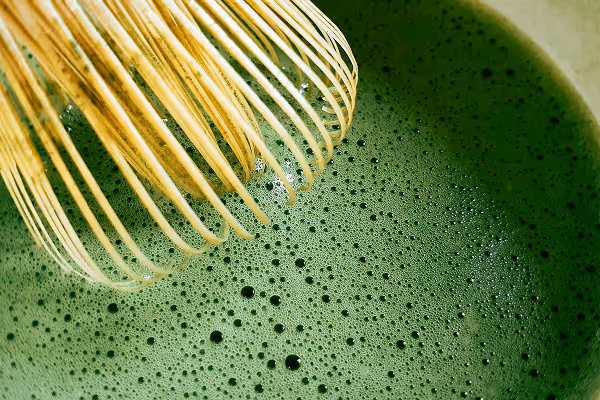 Close up matcha drink with a bamboo whisk on top of it